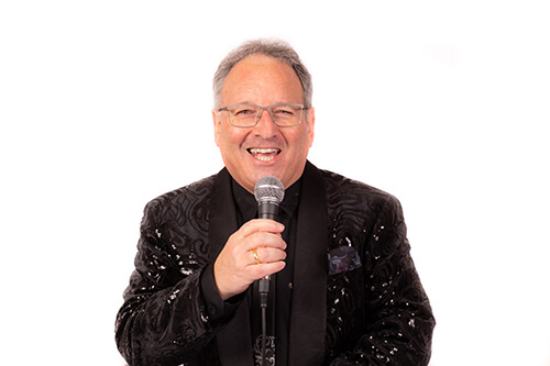 Charles Nove in a black sparkly jacket presenting at a live event. Cutout photo - no background.